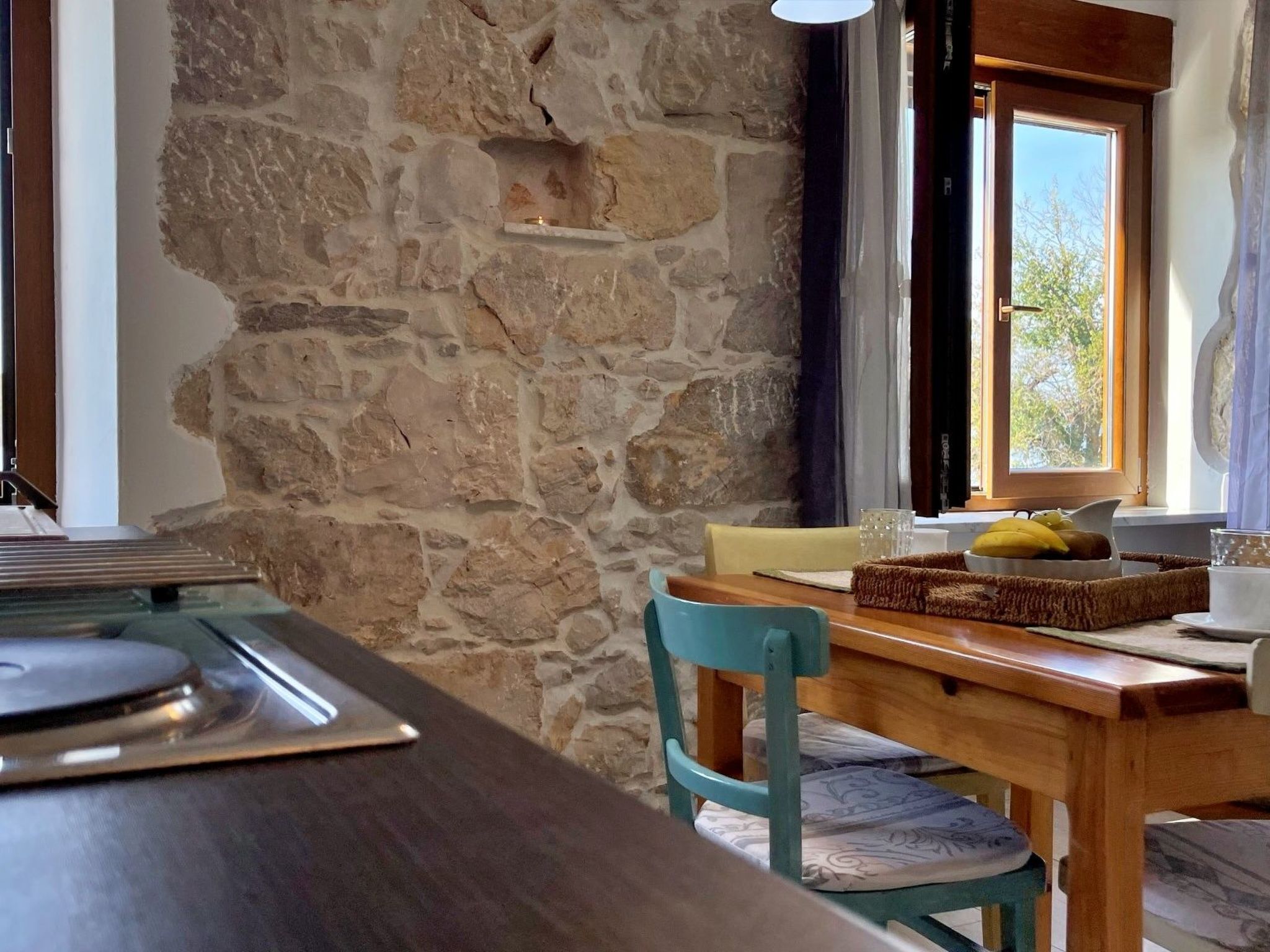A stone wall, wooden table, and a window with a view of trees.