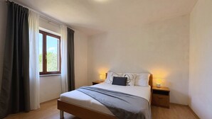 Een slaapkamer met een houten bed, twee nachtkastjes met lampen, een raam met gordijnen en een lamp aan het plafond.