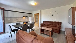 Een moderne woonkamer met een bruine bank, een salontafel en een eethoek met een tafel en stoelen.