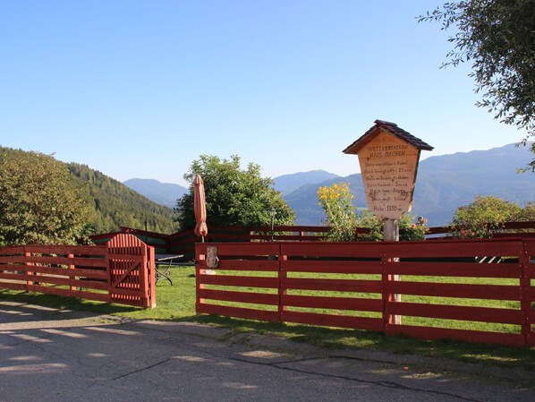 A wooden sign with text, a red gate, and a bench in a scenic outdoor setting.
