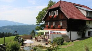 Een rustieke chalet met een schuin rood dak, houten gevel en een kleine tuin met een vijver en tuinmeubilair.
