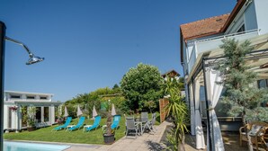 Un espace piscine avec des chaises longues, un petit jardin et un bâtiment doté d’un toit en tuiles.