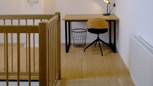 Ein kleines, helles Schlafzimmer im Dachgeschoss mit einem Holztisch, Stuhl und einer kleinen Lampe.