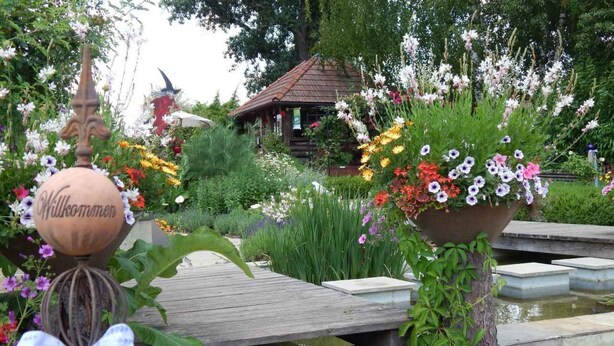Eine Holterrasse mit einem Schild, das 'Willkommen' zeigt, und einer dekorativen Vogelskulptur.