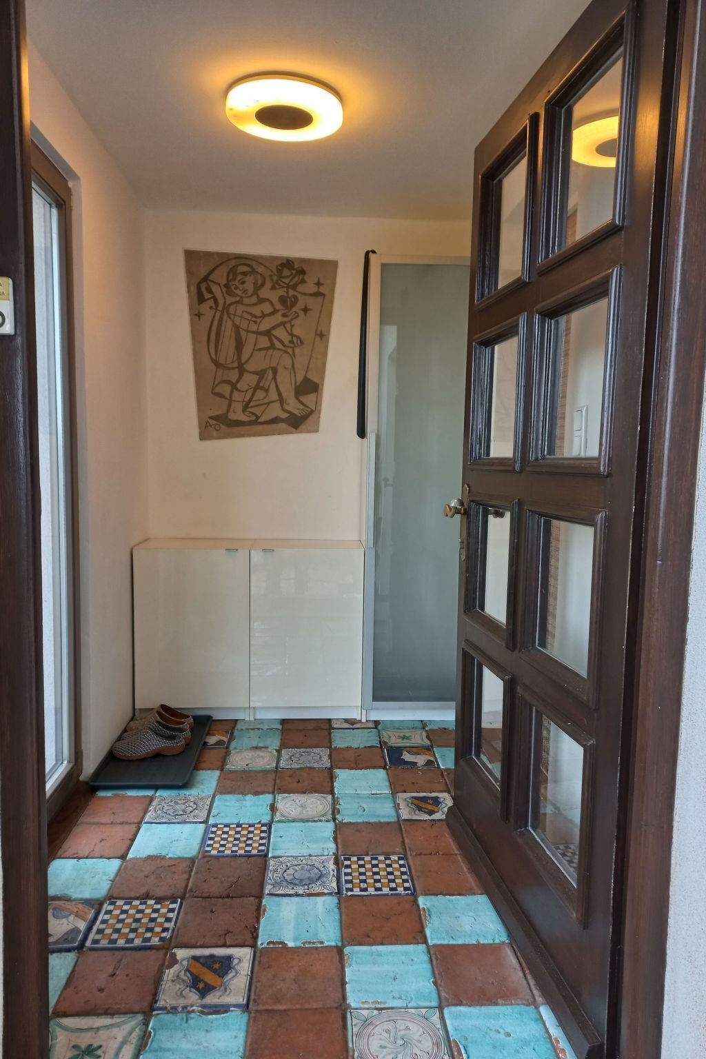 Um corredor com piso xadrez, uma porta com painéis de vidro e uma obra de arte na parede.