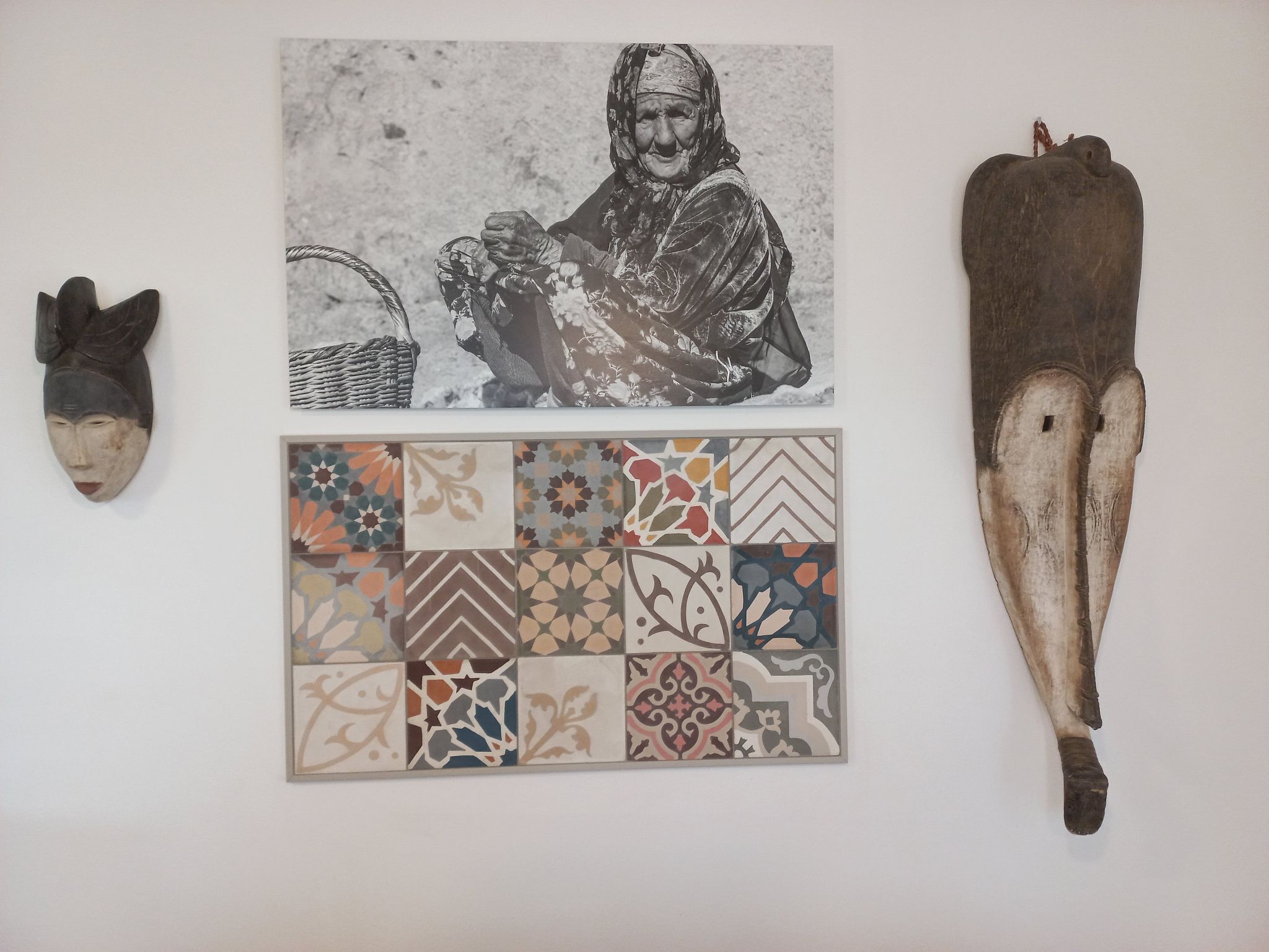 Un muro con una fotografia in bianco e nero, un motivo a maiolica e due oggetti in legno intagliato.