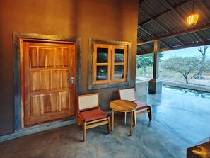 A wooden door and window, two chairs, and a small table in a covered outdoor area with a view of trees. - Yaalu Yaala Safari Camp (Palatupana)