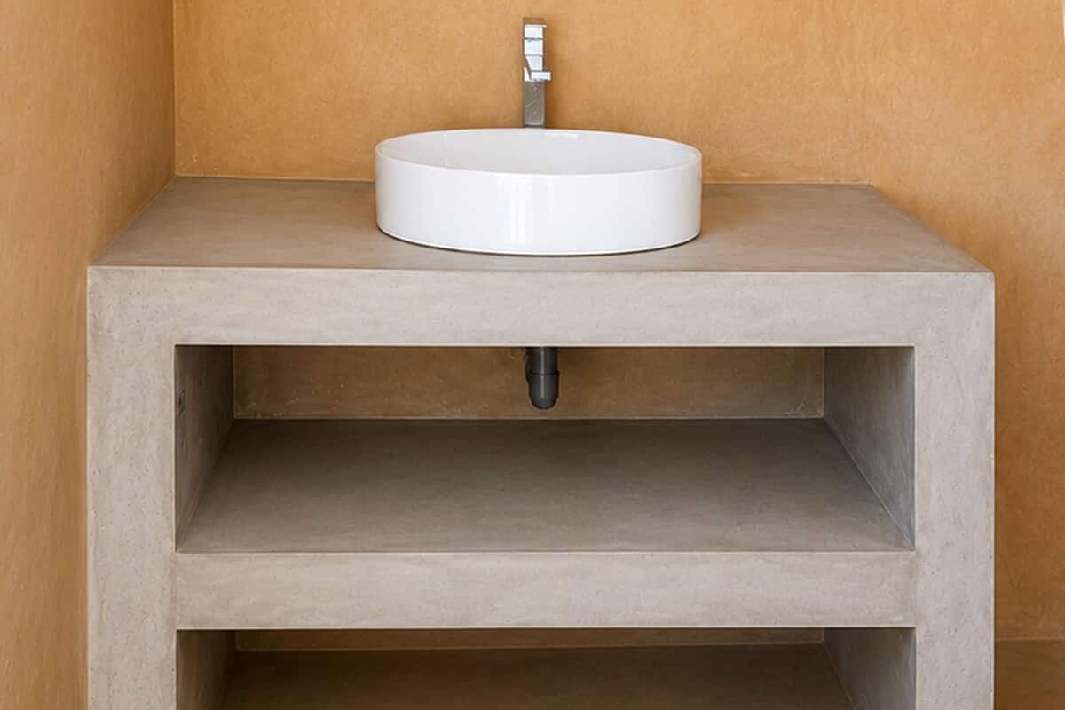 Une salle de bain avec un lavabo blanc, une seule étagère et un mur uni.
