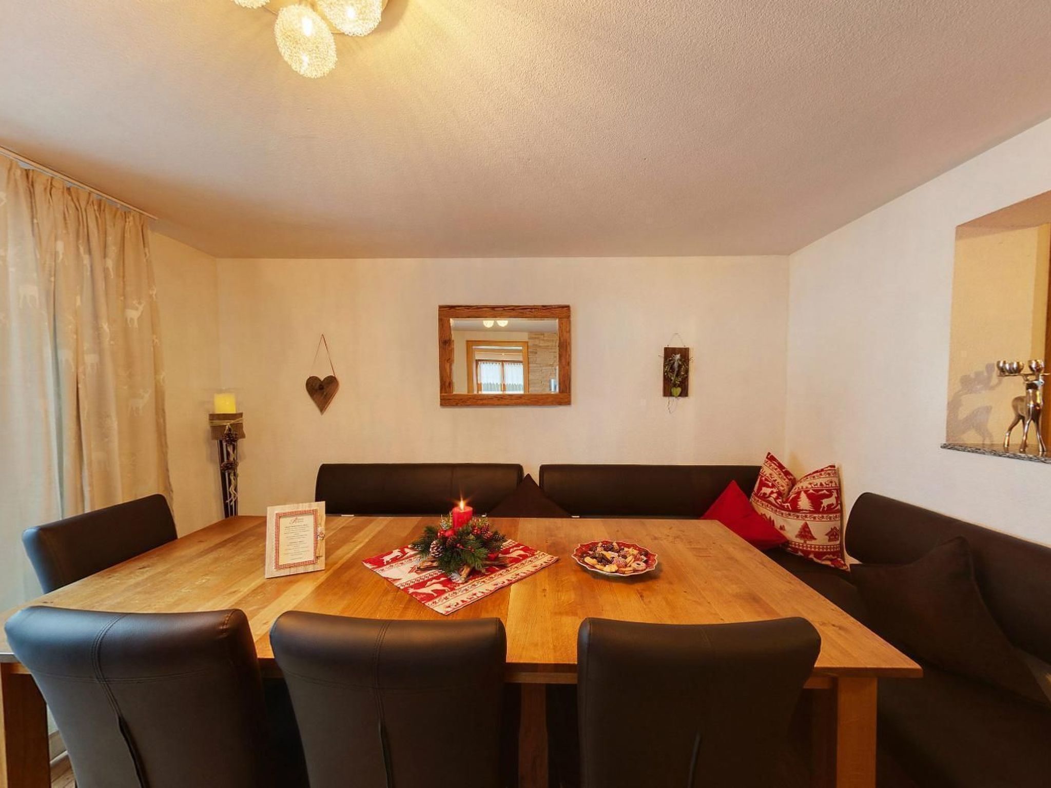Un comedor con mesa de madera, sillas negras y camino de mesa con estampado rojo y blanco.