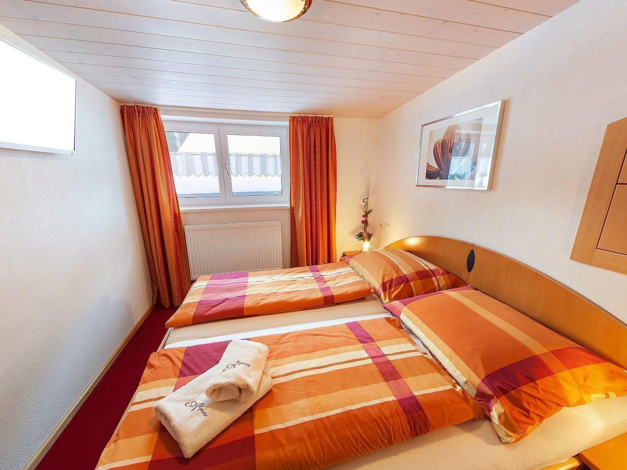 Een hotelkamer met twee bedden, een raam met gordijnen, een radiator en een foto in een lijst aan de muur.