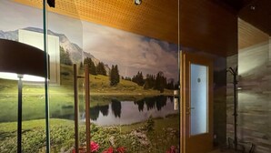 Ein Zimmer mit einer großen Wandmalerei von See, Bergen und viel Grün. Rechts ist eine Tür und links eine Glastrennwand.