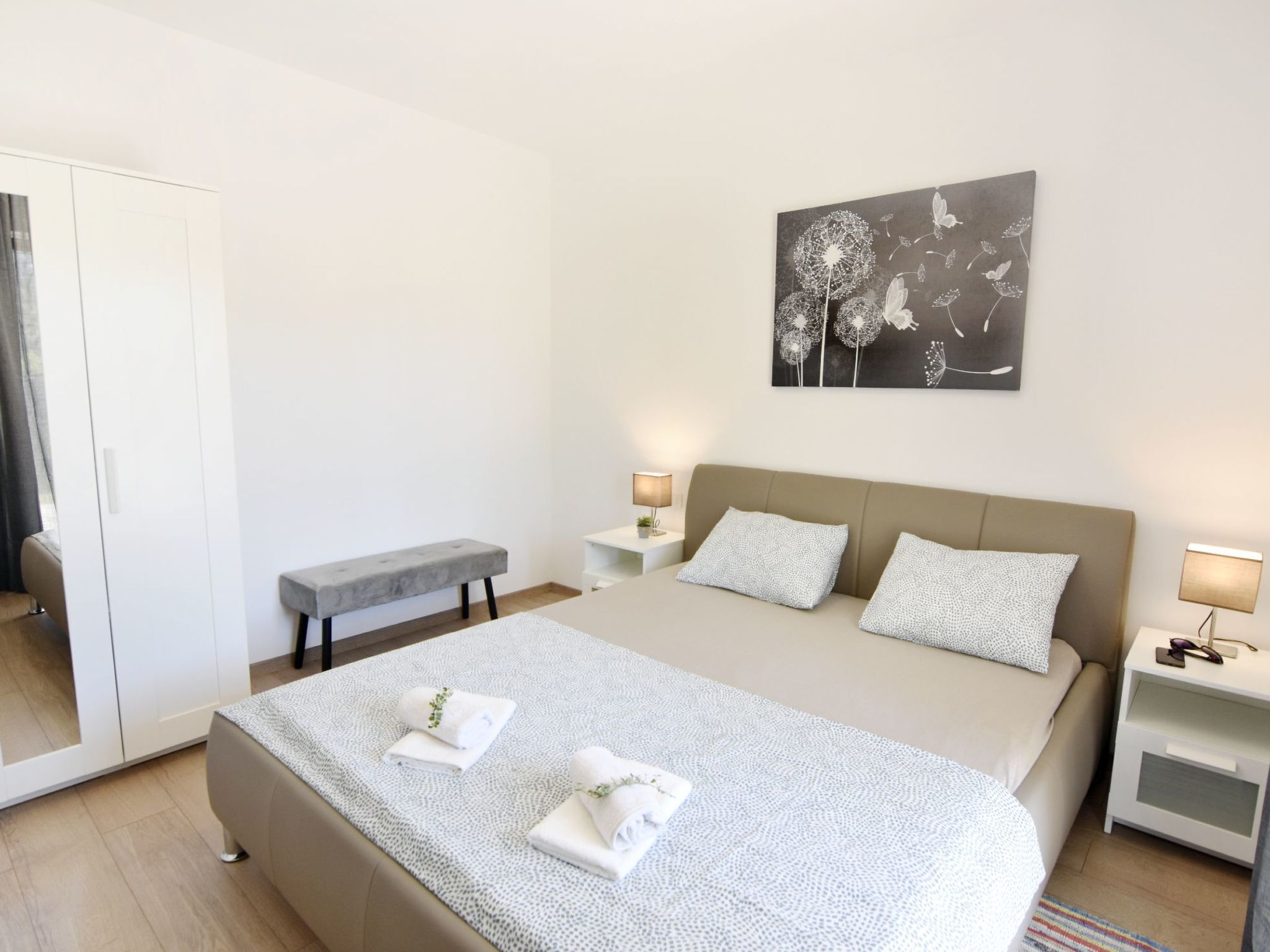 Une chambre à coucher moderne avec un grand lit, deux tables de chevet, un banc et une œuvre d’art accrochée au mur.