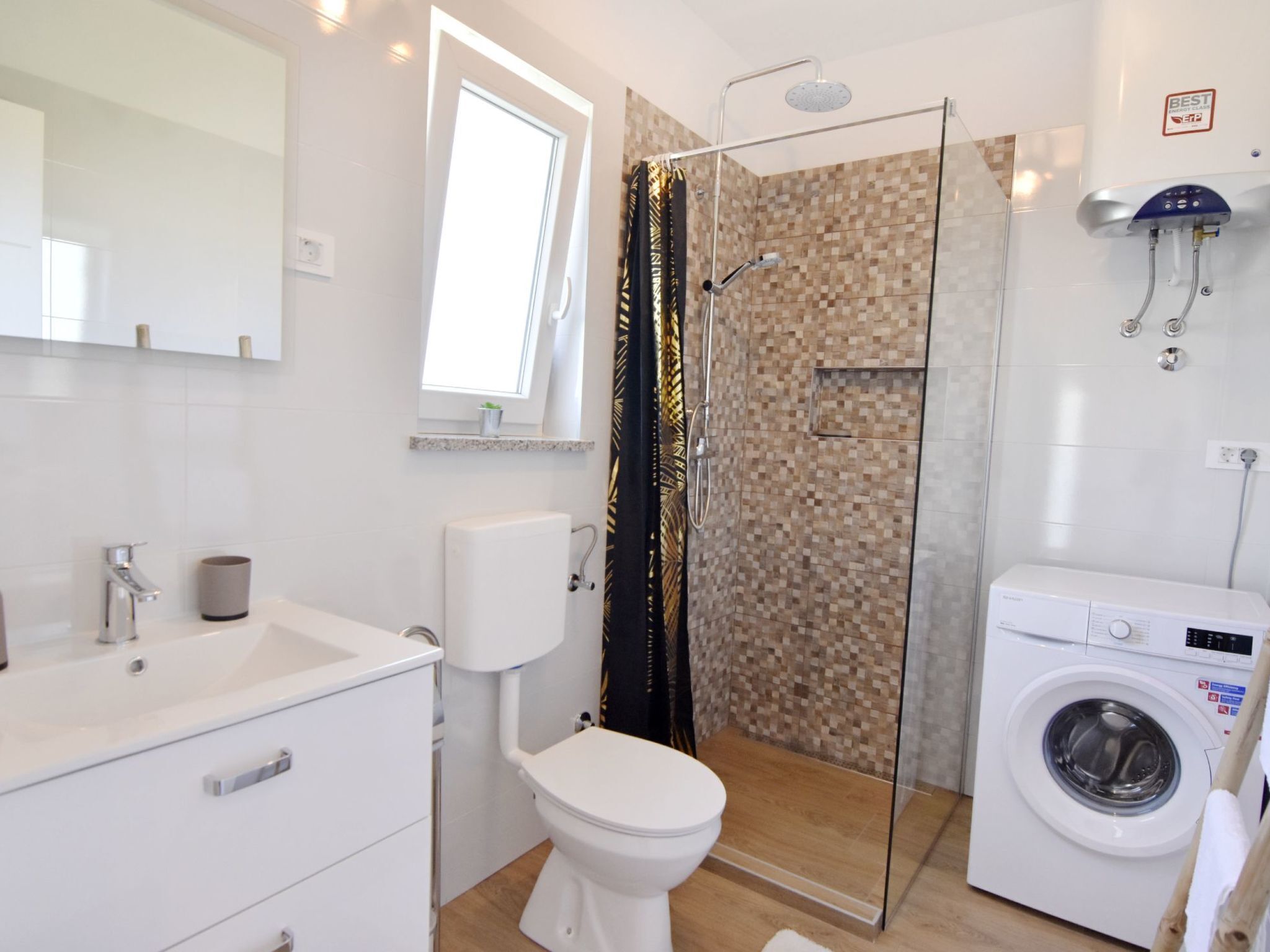 A modern bathroom with a glass shower enclosure, a toilet, a washing machine, and a sink.