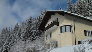 Un edificio de dos pisos con techo inclinado, rodeado de árboles cubiertos de nieve y un cielo despejado.