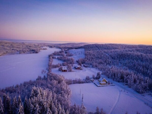 Et snøklædt landskab med en lille hytte og en større bygning, omgivet af tætte skove.