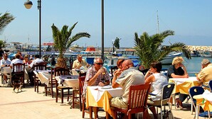 Un área de comedor al aire libre con mesas y sillas, con vista a un puerto deportivo con barcos.