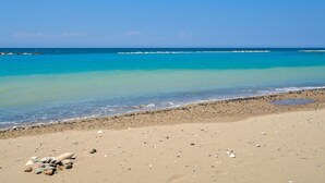Una playa con aguas turquesas cristalinas, una orilla arenosa y un promontorio rocoso a lo lejos.