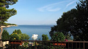 A balcony with a view of the sea, a boat, and surrounding greenery. - Strandnahe Ferienwohnung mit großer Terrasse by Interhome (Brač/Postira)