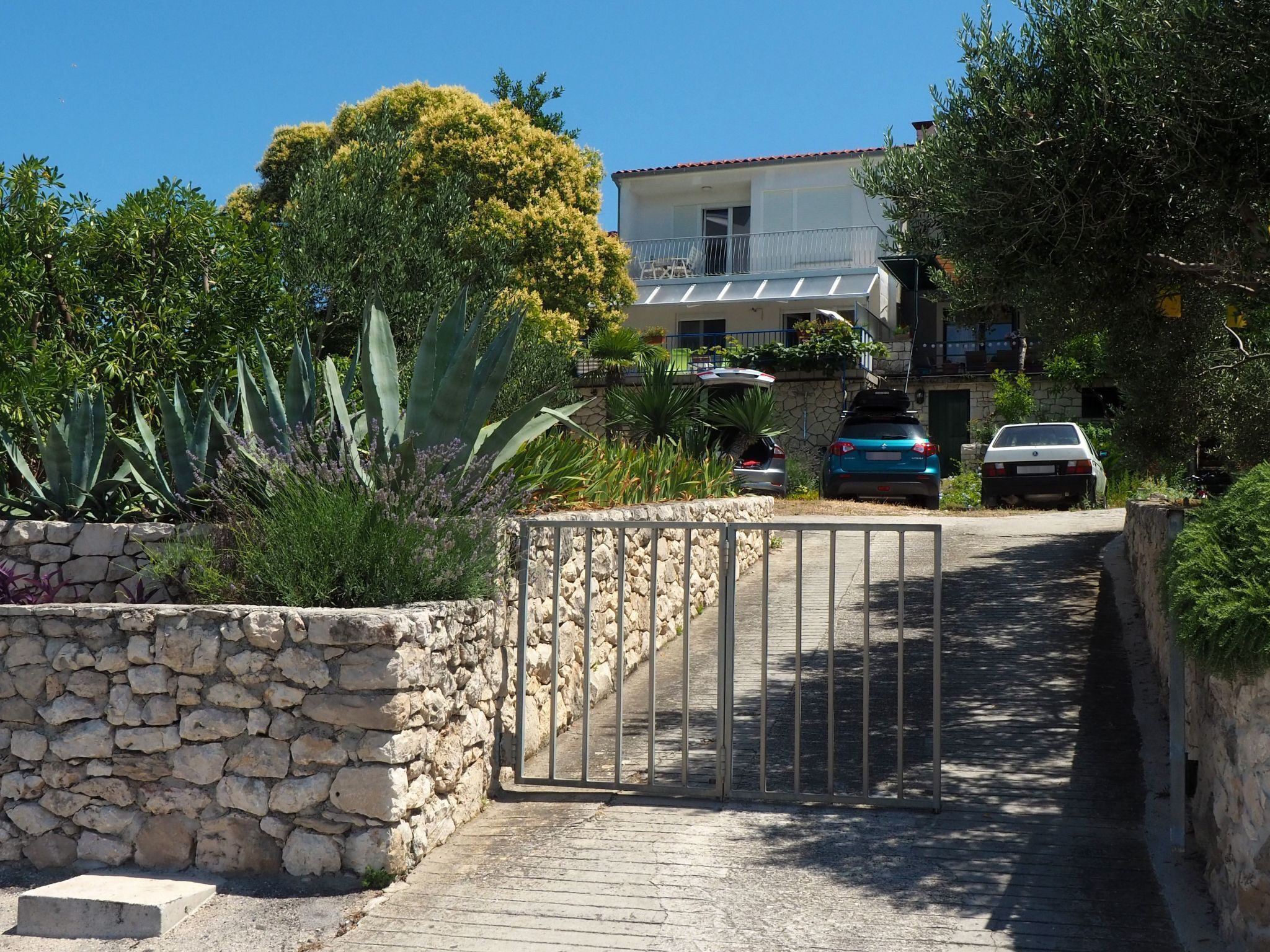 A stone wall, a metal gate, and a paved path leading to a building with a balcony.