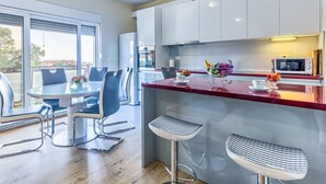 A modern kitchen with white cabinets, a red countertop, and a dining area with two chairs and a table.