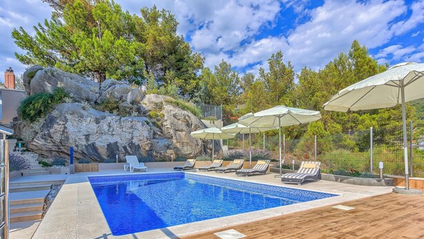 A swimming pool with lounge chairs and umbrellas, surrounded by a wooden deck and greenery.