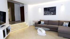 Ein modernes Wohnzimmer mit Flachbildfernseher, einer Couch, einem Couchtisch und einer Treppe, die in einen anderen Raum führt.