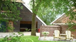 En rustik byggnad med ett sluttande tak, en tegelvägg och ett stort träd framför. Utanför står två Adirondack-stolar.