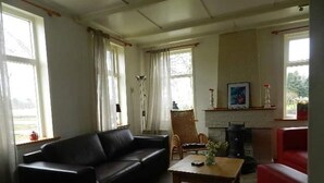 Ett vardagsrum med en svart soffa, ett träbord och en röd fåtölj. Det finns en öppen spis med en dekorativ list ovanför och en tavla som hänger ovanför den.