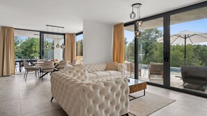 A spacious living room with a large tufted sofa, a dining area with a table and chairs, and large windows offering a view of the outdoors. - Sunset Villa Santalezi by Interhome (Nedescina)