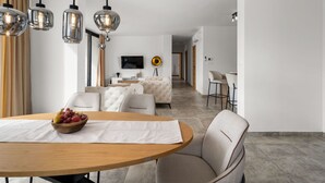 A modern living room with a wooden dining table, a sofa, and a TV in the background. - Sunset Villa Santalezi by Interhome (Nedescina)