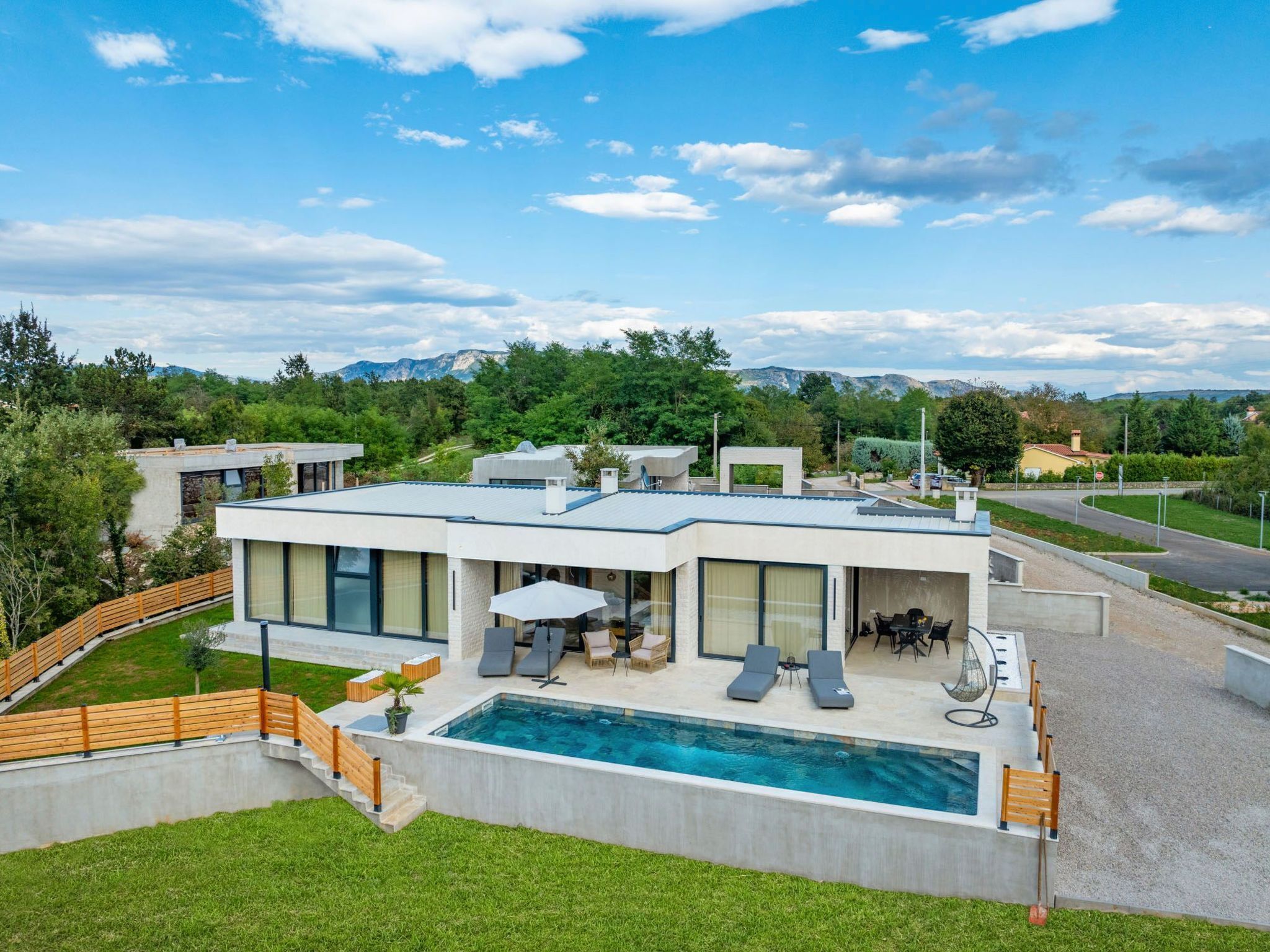 A modern house with a swimming pool, outdoor seating, and a view of the surrounding landscape.