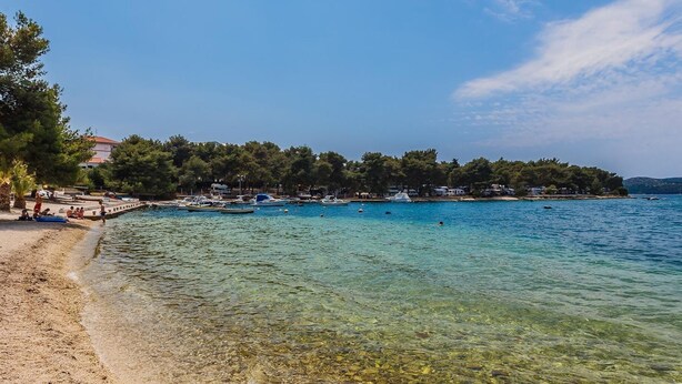 Una playa con aguas cristalinas y poco profundas, barcos y una orilla bordeada de árboles.