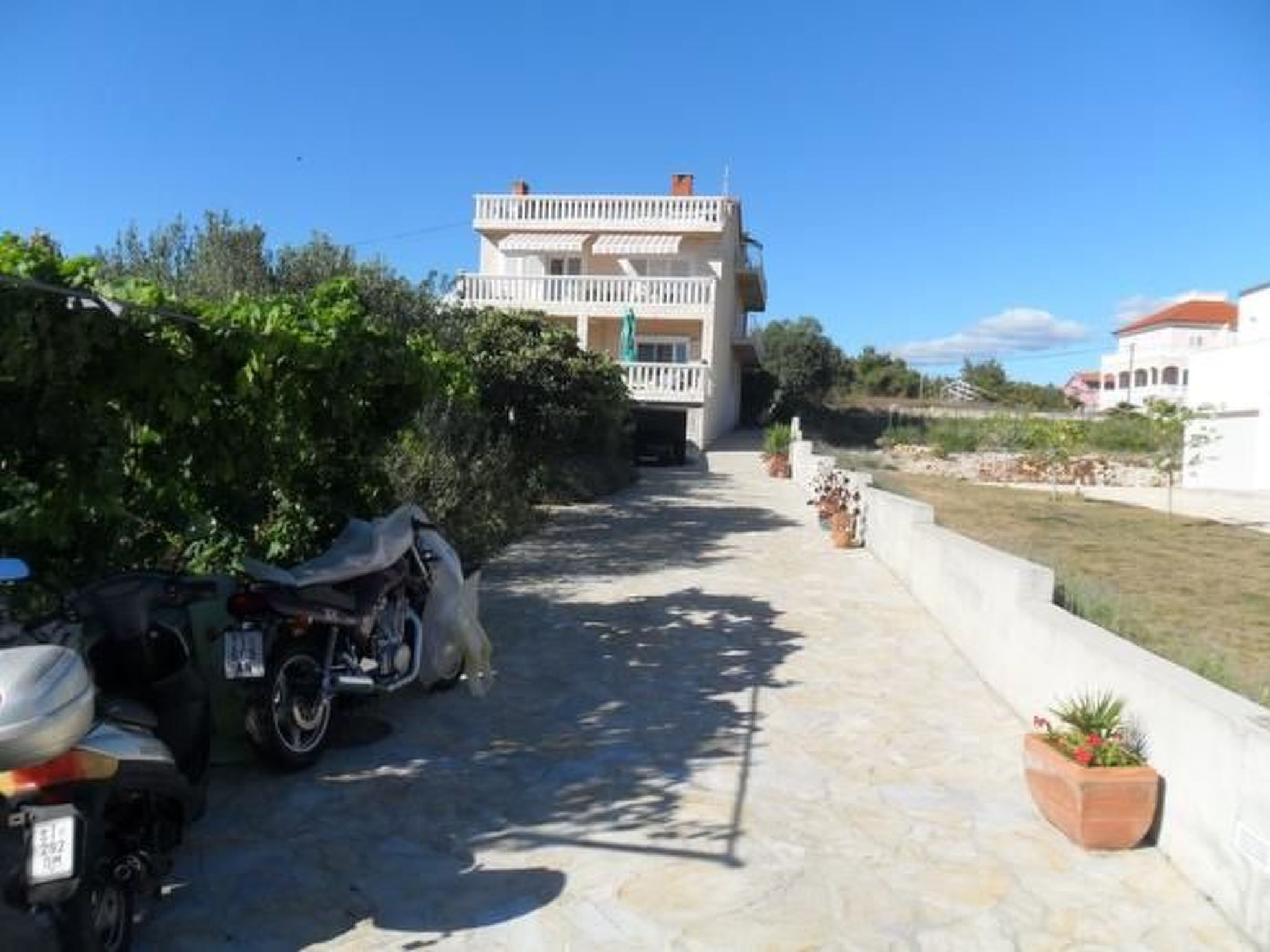 Ein zweistöckiges Gebäude mit einem Balkon, einer gepflasterten Auffahrt und einem abgestellten Motorrad.