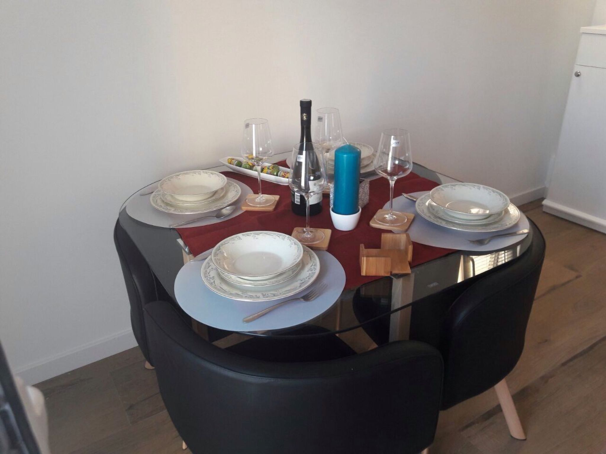 A dining table set with plates, glasses, and a bottle, surrounded by chairs.
