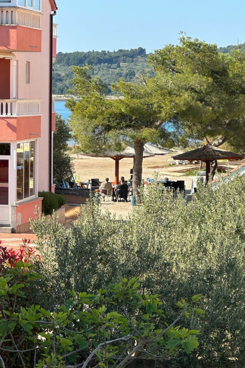 A building with a balcony overlooking a beach area with outdoor seating and umbrellas.
