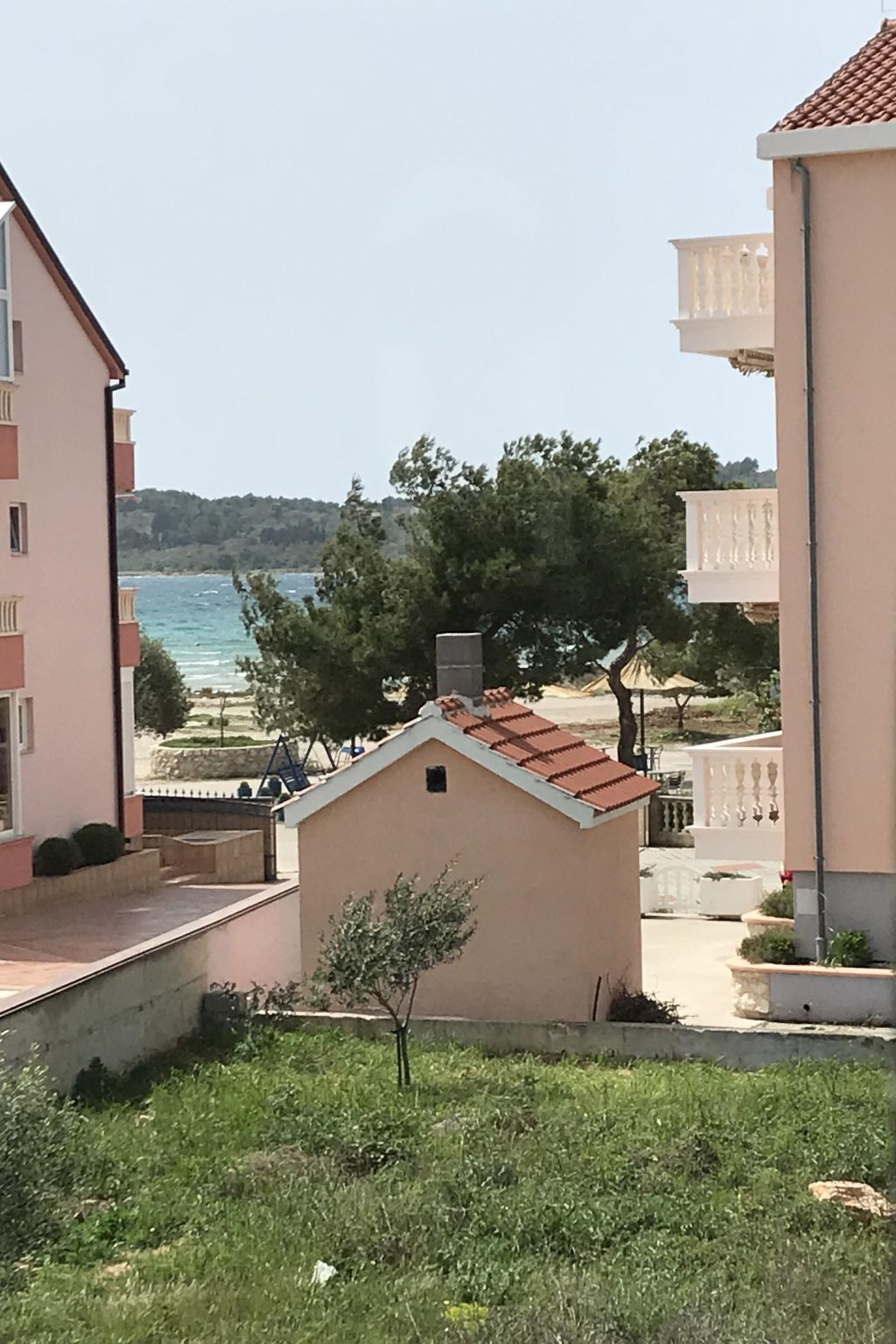 A coastal residential area with buildings, a small structure with a red roof, and a view of the sea.