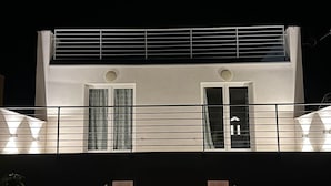 Een modern gebouw met een plat dak, grote ramen en een balkon met hekwerk.
