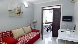 Un saló modern amb un sofà de quadres vermells i blancs, una taula de dinar amb cadires, un televisor fixat a la paret i una porta que dona a una zona exterior.
