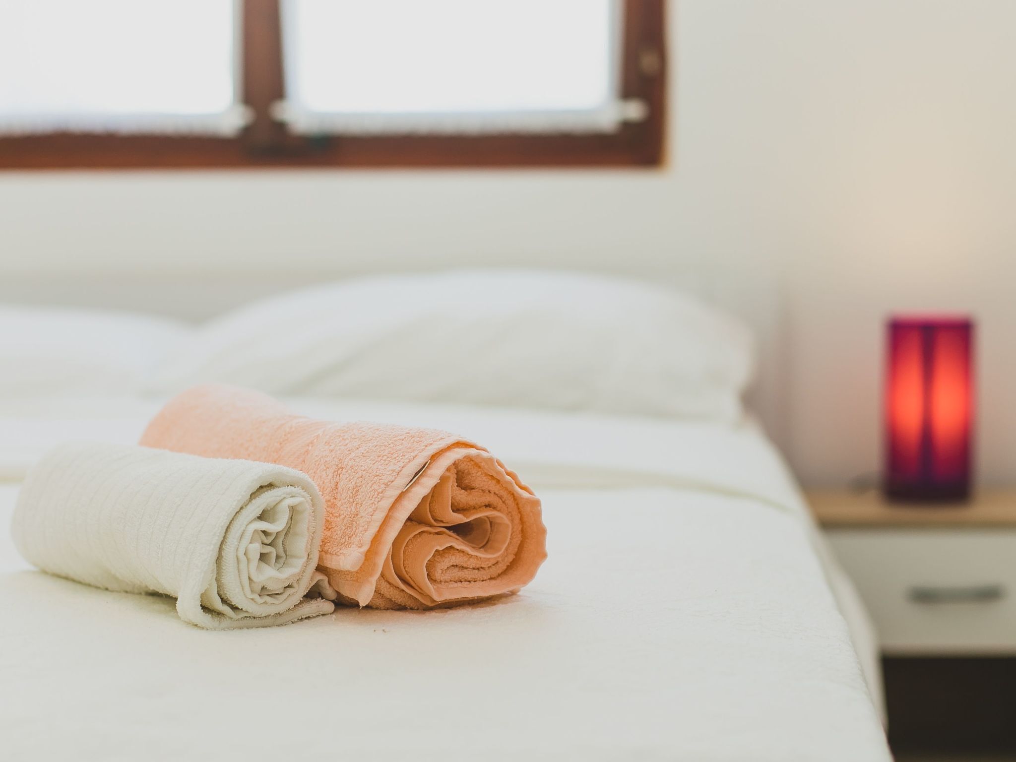 A neatly made bed with folded towels and a bedside table with a red candle.