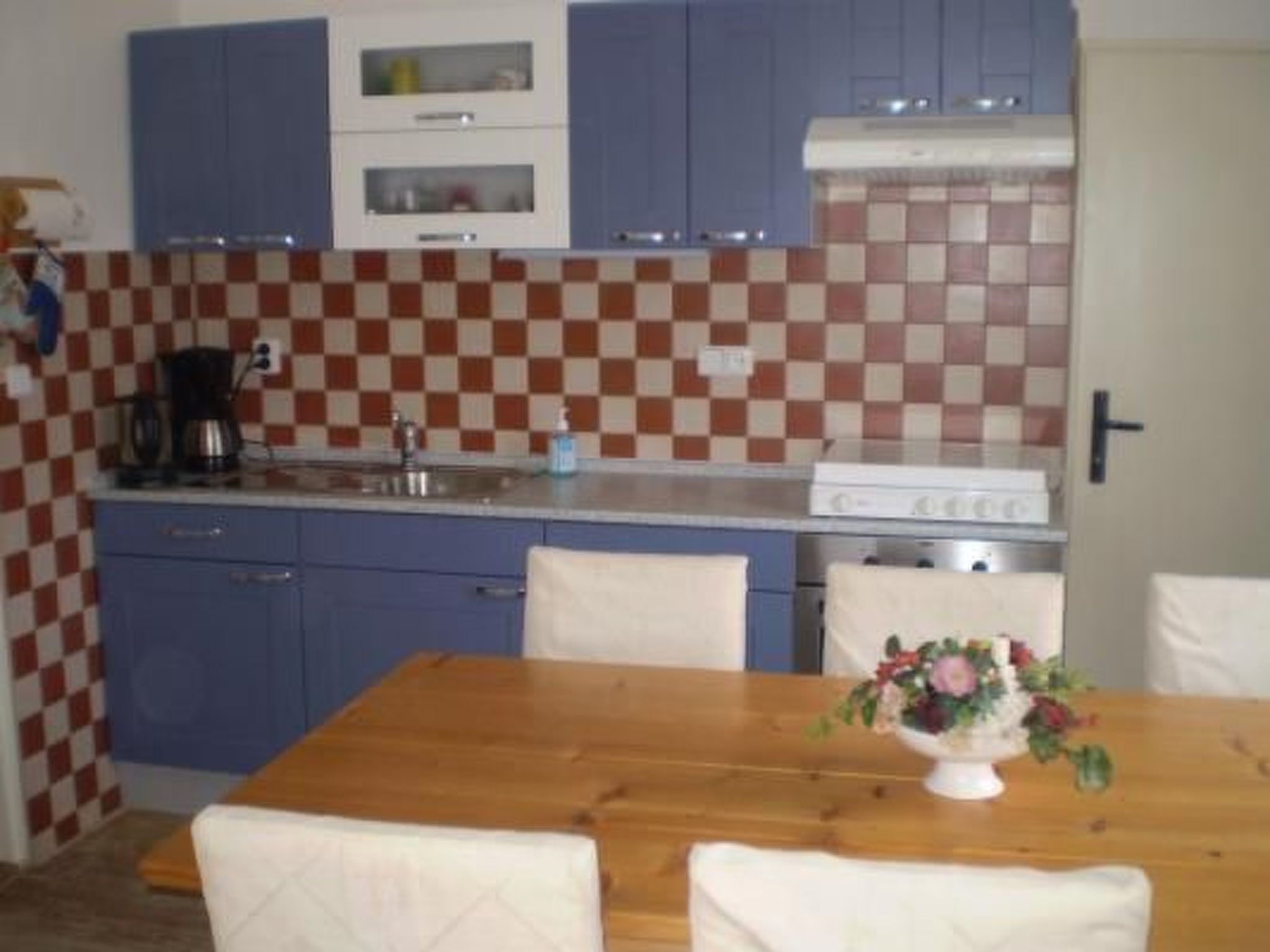 Una cocina con armarios azules, un respuesto a cuadros, una mesa de madera con sillas y una estufa.