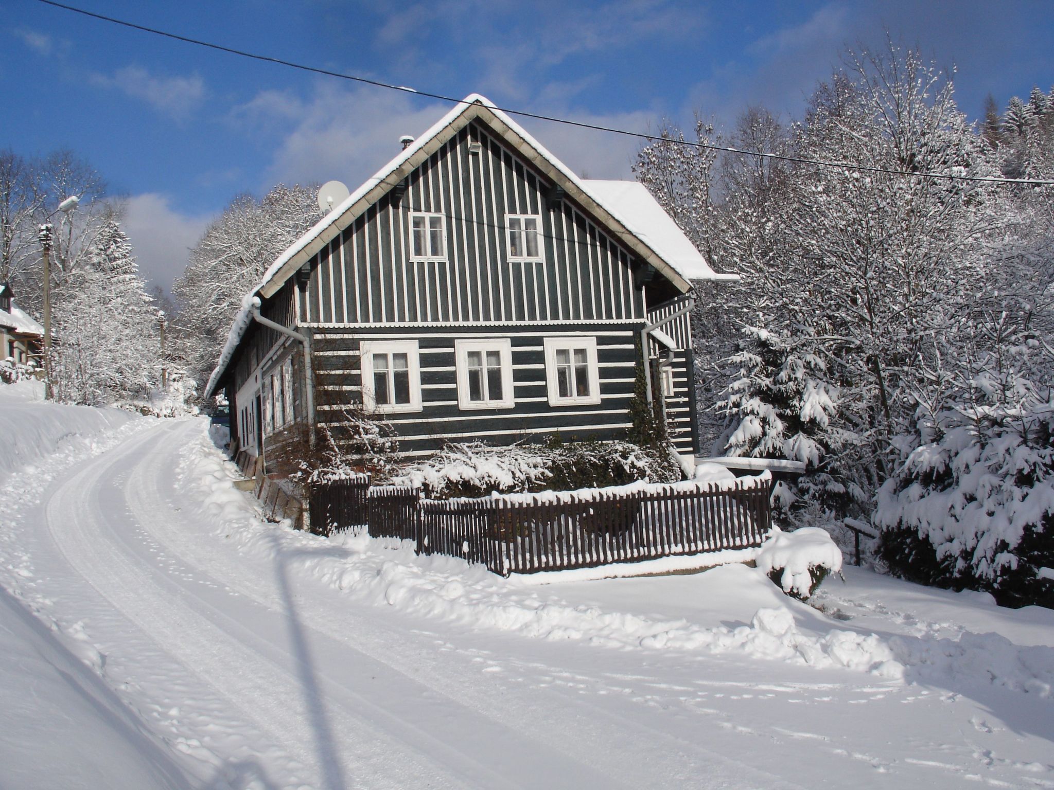 A wooden house with a snow-covered roof and a wooden fence in front.