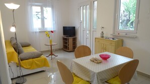 Un espacio habitable compacto con sofá, mesa de comedor, sillas, televisor y una mesita auxiliar.