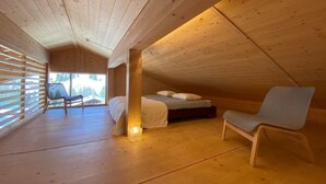 Ein gemütliches Schlafzimmer im Dachgeschoss mit Bett, Stuhl und Fenster mit Blick auf einen Wald.
