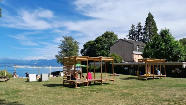 An outdoor area with wooden structures, a grassy field, and a building in the background.