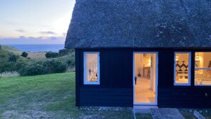 Ein reetgedecktes Häuschen mit Holzfassade, einem sichtbaren Innenraum mit Essbereich und Blick auf das Meer.