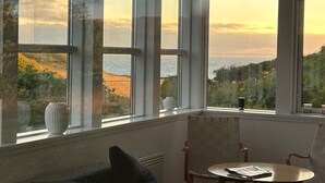 Ein Zimmer mit großen Fenstern und Meerblick, einem runden Tisch und einem Sessel.