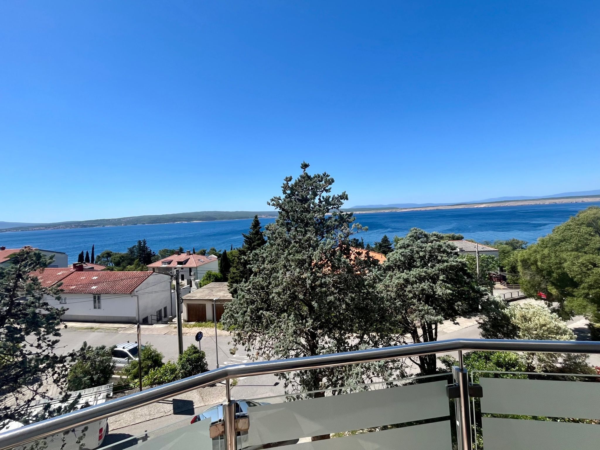 A coastal view from a balcony with a clear sky, a large tree, and buildings in the background.