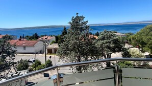 A coastal view from a balcony with a clear sky, a large tree, and buildings in the background.