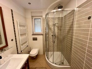 Uma casa de banho moderna com chuveiro de vidro, sanita, lavatório e janela.