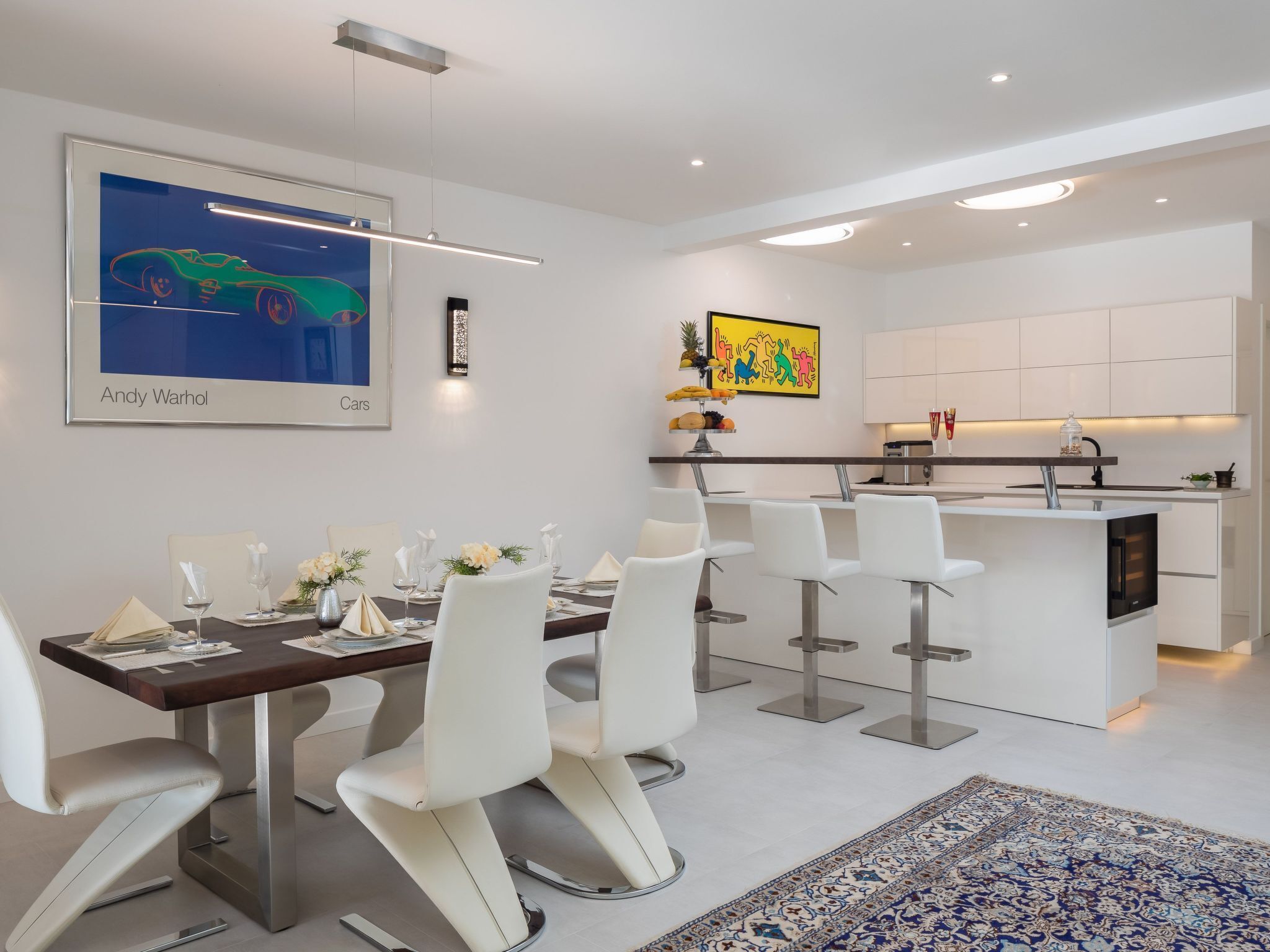 A modern kitchen with white cabinets, a dining area with white chairs, and a colorful artwork on the wall.